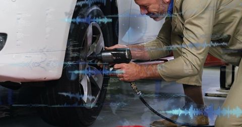 Senior mechanic kneeling torquing front wheel with air wrench in modern repair bay