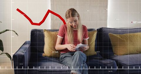 Young woman on blue velvet sofa sorting bills with red declining financial graph overlay