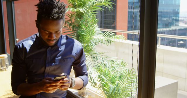 Young man looking at smartphone by window with cityscape view - Download Free Stock Images Pikwizard.com