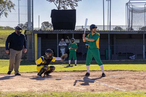 Batter swinging at incoming pitch during amateur baseball game in green uniform