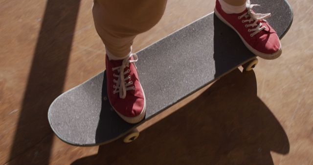 Close-up view of a skateboarder's red sneakers while gliding on a skateboard. This image captures the dynamic nature of skateboarding, highlighting the skateboard deck and the casual, vibrant footwear. Useful for articles, blog posts, advertisements, and campaigns focused on youth culture, action sports, and urban fashion.