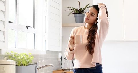 Relaxed woman in bright kitchen with pastel mug