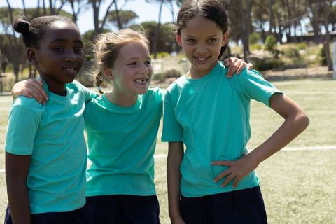 Multiracial girls laughing and supporting each other on sunny youth sports field