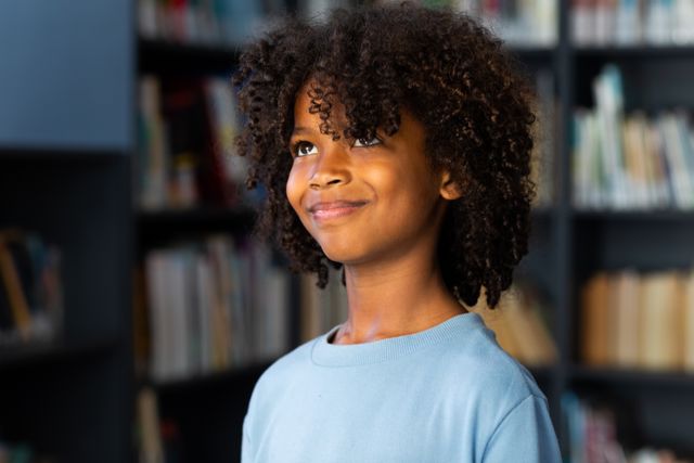Young African American schoolboy with long curly hair smiling in a library. Ideal for educational materials, school promotions, childhood development articles, and learning resources.