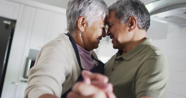 Senior couple enjoying time together, dancing in modern kitchen. Perfect for depicting love, romance, aging gracefully, and healthy lifestyle in older age advertisements or editorial content.