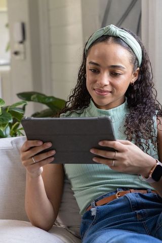 African american woman relaxing on sofa using tablet for remote learning and reading