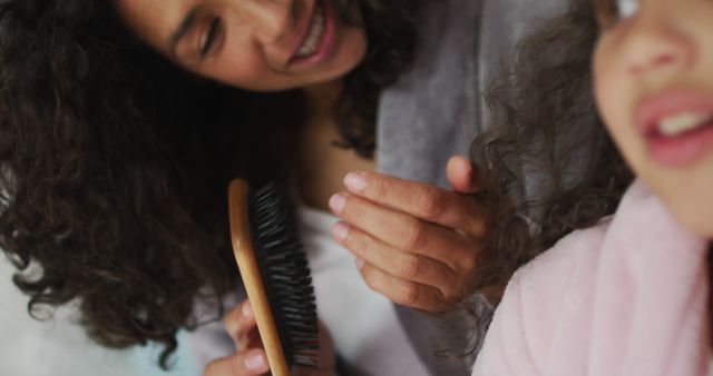 Happy biracial mother and daughter brushing hair in bedroom. domestic life and family leisure time concept.