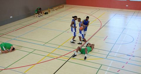 Midcourt basketball drama: blue team holding ball while opponents recover on hardwood