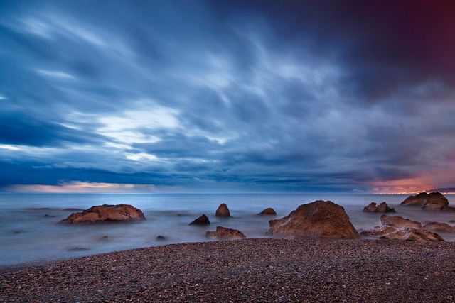 Tranquil seascape featuring large rocks with a dramatic, cloudy sky at twilight. Perfect for backgrounds, calming visual content, travel and tourism materials, and nature-themed designs.