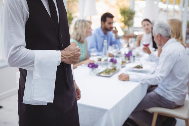 Waiter standing with napkin while friends dining in background