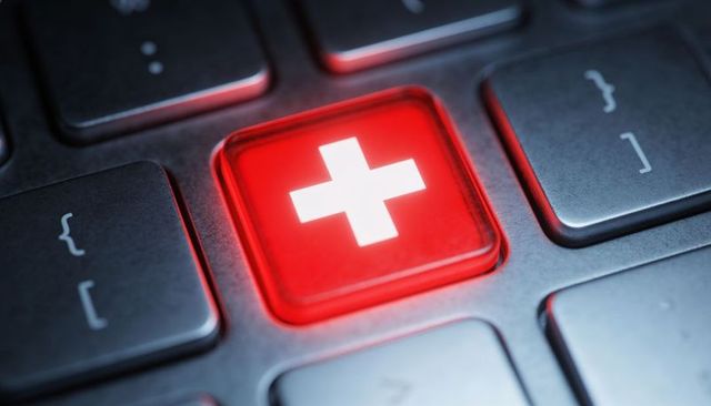 Glowing red medical cross key on backlit keyboard representing telehealth and cybersecurity