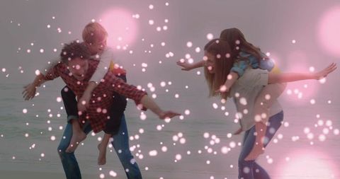 Parents giving piggyback rides on sandy beach with playful kids and dreamy pink bokeh