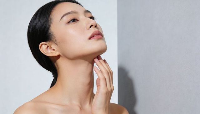 Minimal dewy skin portrait of asian woman tilting head, touching neck, bare shoulders clean beauty