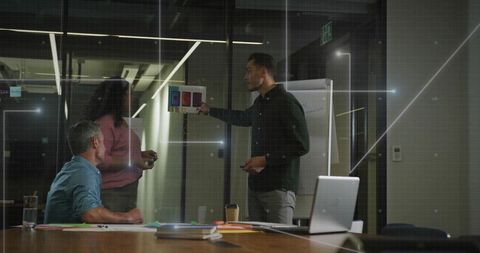 Presenter pointing at color mockups on glass wall during team collaboration in office