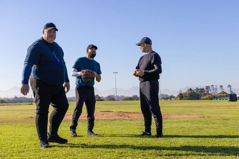 Mature coaches coaching baseball practice on sunny field with glove and whistle