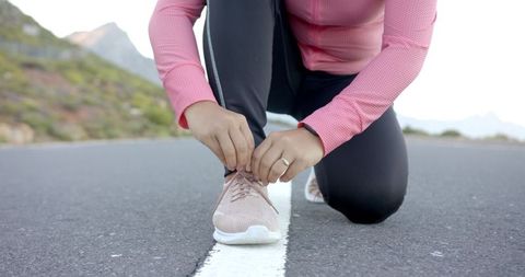 Woman Tying Shoelaces on Mountain Road Before Hike