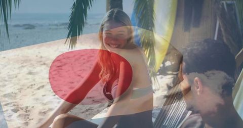 Smiling couple relaxing under cabana on tropical beach with hammock and palm fronds