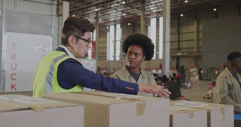 Warehouse manager pointing and training team over labeled shipping boxes at loading dock
