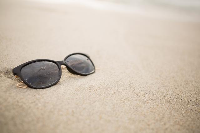 Sunglasses resting on sandy beach, perfect for themes related to summer vacations, beach holidays, and relaxation. Ideal for travel blogs, vacation advertisements, and lifestyle magazines.