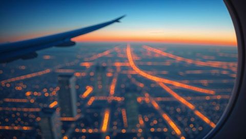View of city streets and airplane wing at twilight from cabin window