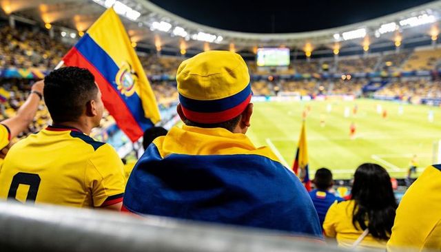 Colombian fans cheering in night stadium wearing yellow jerseys and waving national flag