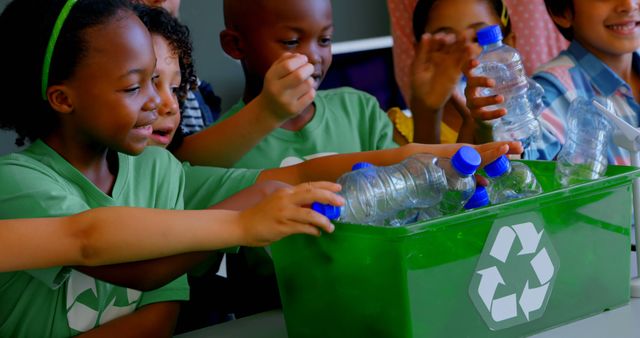 Diverse group of children enthusiastically disposing plastic bottles into recycling bin. Children wearing green shirts highlighting environmental responsibility. Ideal for content focusing on environmental education, sustainability, teamwork, and diversity.
