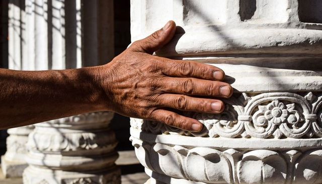 Resting veiny hand on carved white marble pillar showing lotus band and ornate detail at temple