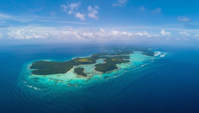 Aerial turquoise archipelago with fringing reefs and sailboat navigating shallow lagoons