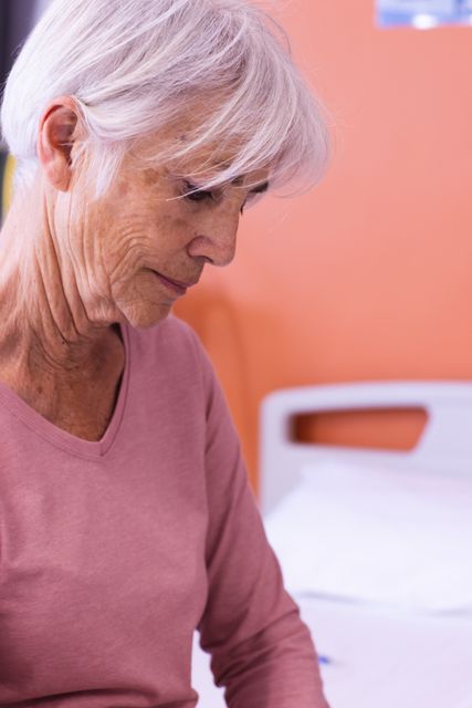 Vertical of smiling senior caucasian female patient sitting on hospital bed looking down. Medical services, hospital and healthcare concept.