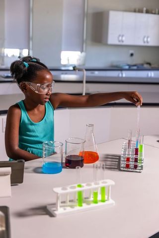 African american girl conducting colorful chemistry experiment in school stem laboratory
