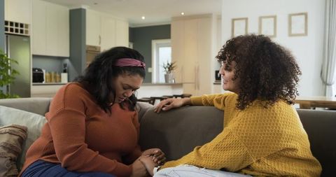 Female friends comforting on couch, holding hands, sharing empathy and emotional support