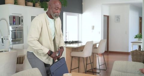 African mature man packing navy briefcase in modern bright minimalist kitchen
