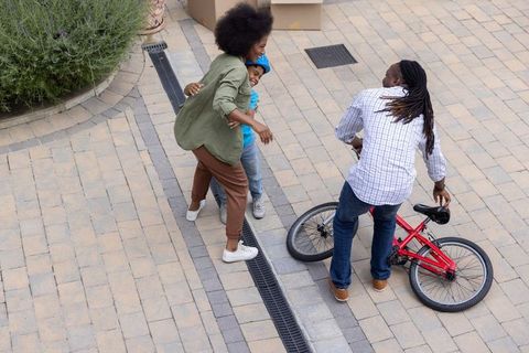 African american parents teaching son to ride bike on paved courtyard, family hugging