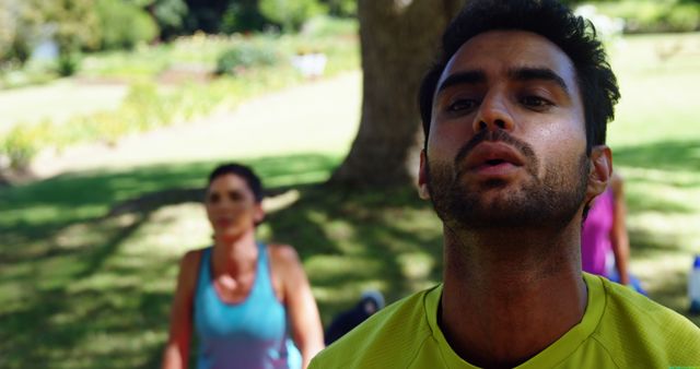 Young man engaged in exercise routine during summer in a park. Can be used for topics related to fitness, outdoor activities, healthy living, and exercise motivation in public spaces.