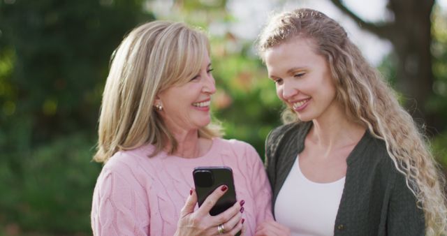 Image of happy caucasian senior mother and adult daughter looking at smartphone in garden. Family, domestic life and togetherness concept digitally generated image.