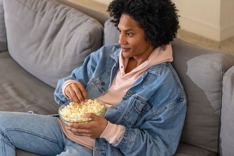 African american man lounging on grey sofa enjoying popcorn and cozy home leisure