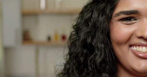 Closeup portrait indian woman smiling with glossy lips and teeth in warm kitchen bokeh
