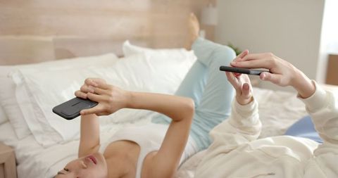Friends Relaxing on Bed and Engaging with Smartphones