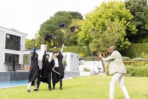 Graduates tossing caps poolside celebrating diploma moment friend taking phone