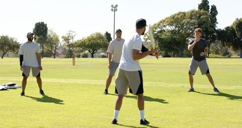 Friends playing cricket on sunny park field showing batting, bowling, teamwork, leisure