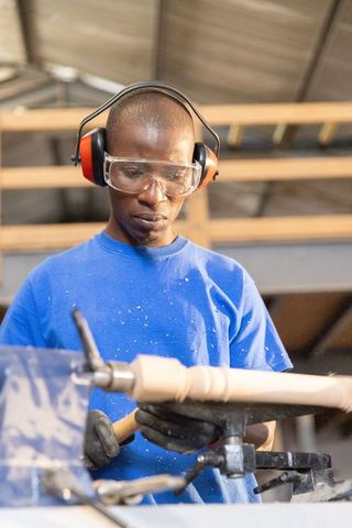 African american craftsman shaping wooden spindle on lathe wearing goggles and earmuffs