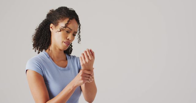 Young woman experiencing discomfort in her wrist, wearing a casual blue shirt, looking concerned. Useful for health articles, medical blogs, wellness content, or injury prevention campaigns.