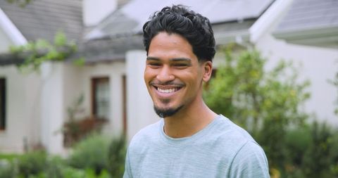 Smiling young man standing in front yard of neighborhood home