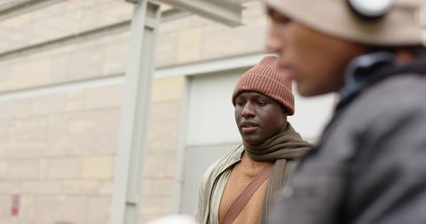 Young commuters waiting at urban transit shelter wearing beanies, scarves, headphones