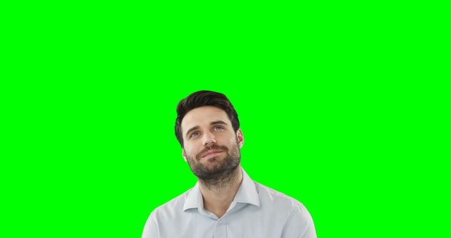 This image features a man with a beard looking up thoughtfully against a green screen background. The green screen is perfect for keying in various backgrounds, making it ideal for creative projects, advertising, or social media. The thoughtful expression on the man's face can be used to convey ideas, inspiration, or decision-making contexts for businesses and promotional content.