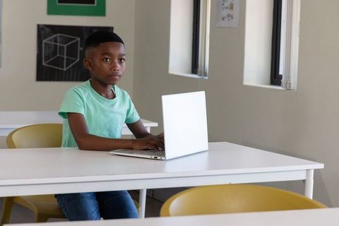 Focused african american boy using laptop in bright classroom for digital learning