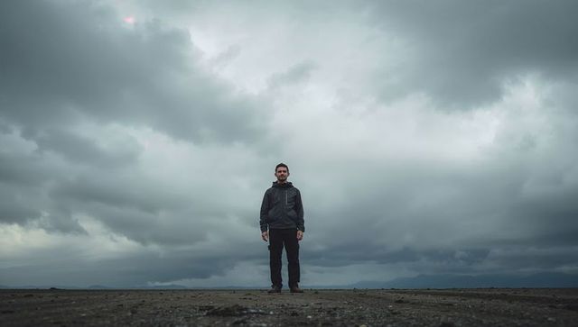 Standing hiker on tidal flat under dramatic storm clouds conveying solitary resilience
