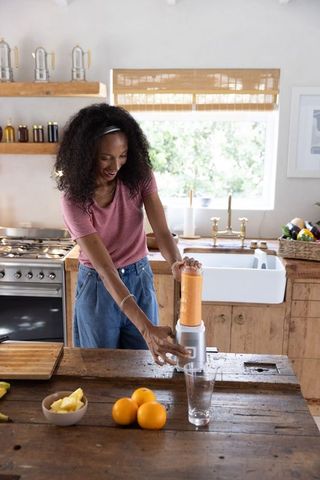 African american woman blending orange smoothie at farmhouse kitchen island