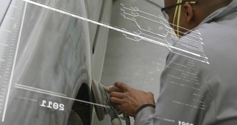 Technician sanding car panel using orbital sander wearing safety glasses in workshop