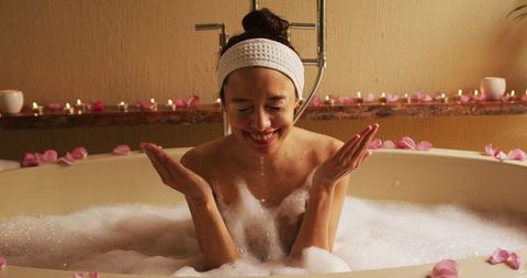 Woman enjoying relaxing bath with foam and rose petals